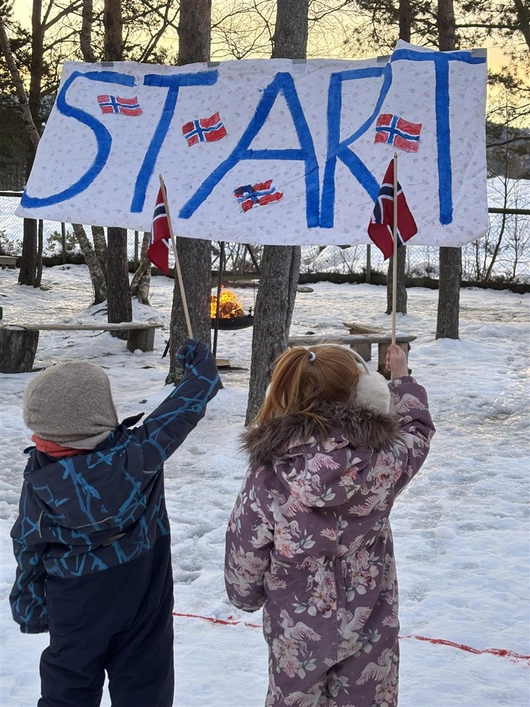 To barn står med ryggen til og vifter med norske flagg. De har en plakat hvor det står "start" på foran seg.  - Klikk for stort bilde