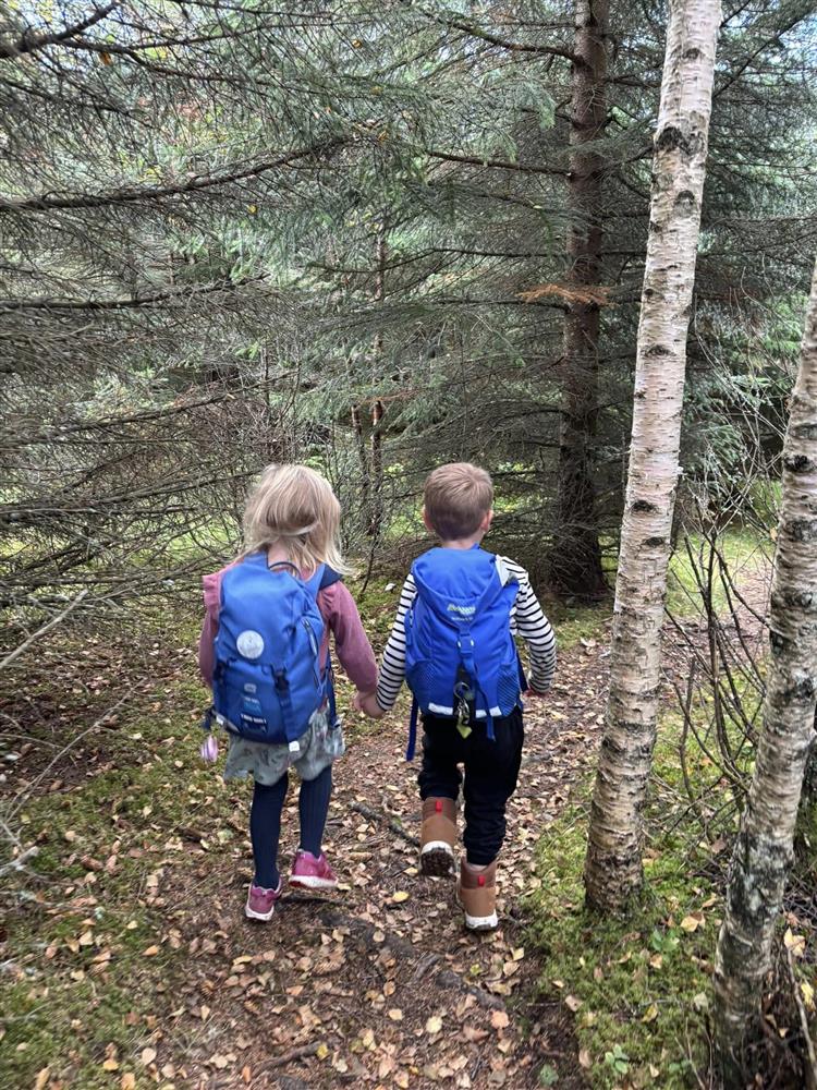 To barn holder hender mens de går tur i skogen. Begge har blå sekk på ryggen.  - Klikk for stort bilde