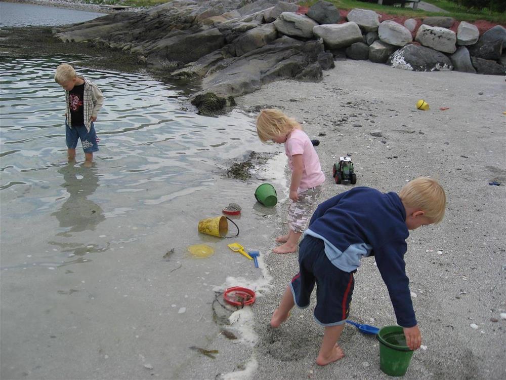 tre barn leker i fjæra med sand og bøter - Klikk for stort bilde